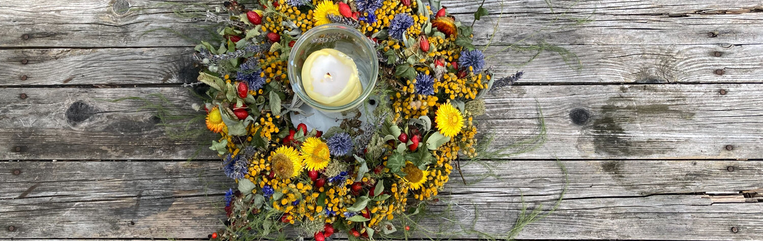 Zelfgebonden kleurrijke herfstkrans van bloemen en bessen met windlicht op een houten tafel