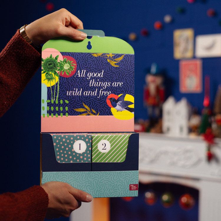 Geopende zaad-adventskalender „Groenten, kruiden & bloemen” met zakjes 1 en 2, in handen gehouden