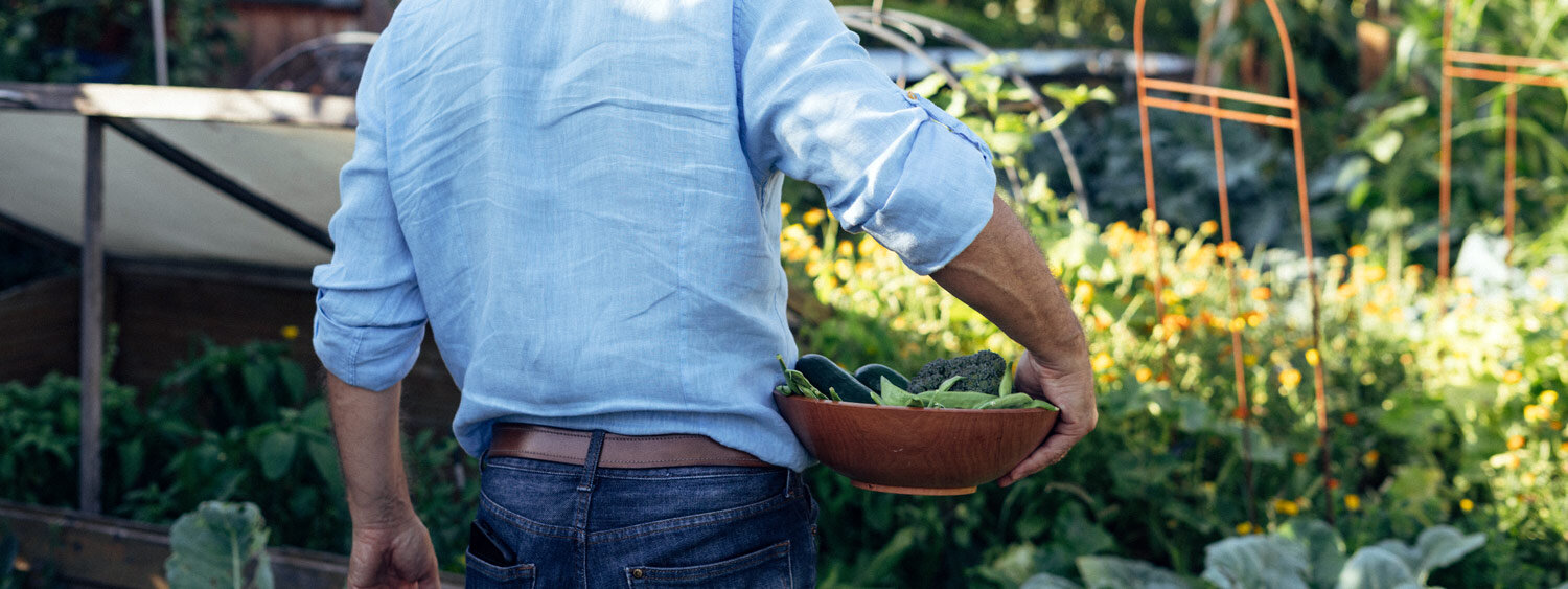 Tuinier draagt een schaal met vers geoogste bladgroenten door de moestuin