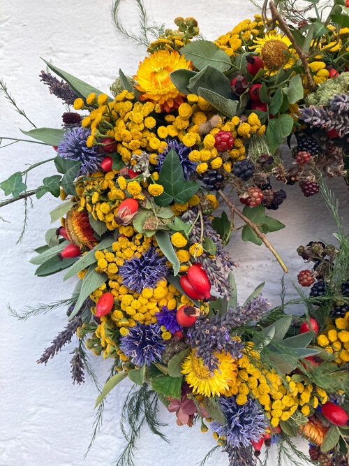 Detail van een herfstkrans met gele en blauwe bloemen, rode rozenbottels en donkere bessen
