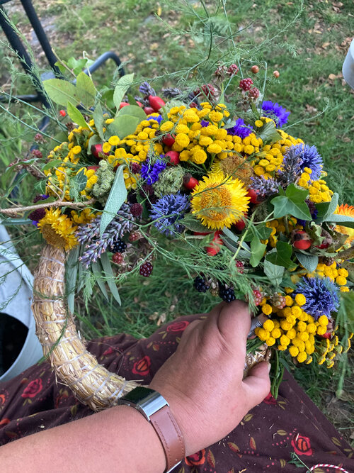 Half gebonden herfstkrans van gele en blauwe bloemen, grassen en bessen op een strokrans