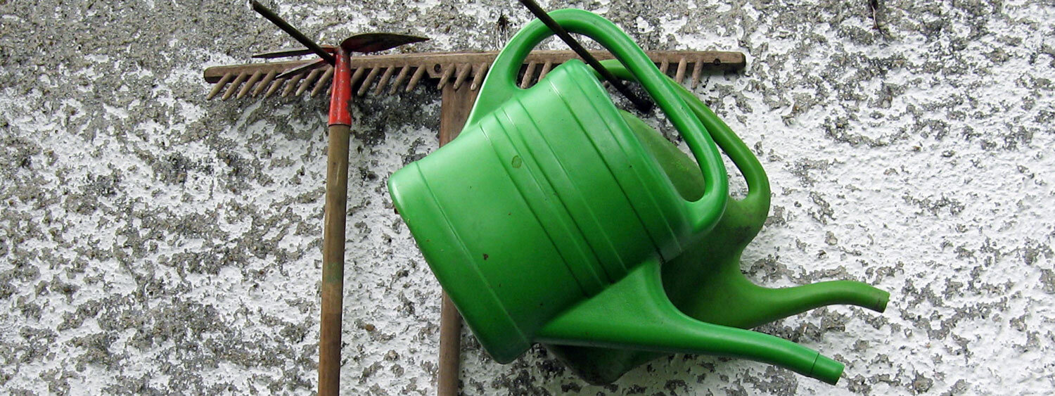 Twee groene gieters en een hark hangen aan een muur