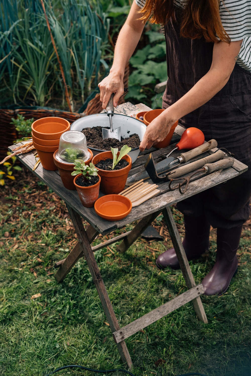 Tuinierster vult aan de tuintafel kleine terracotta potjes met aarde om te zaaien